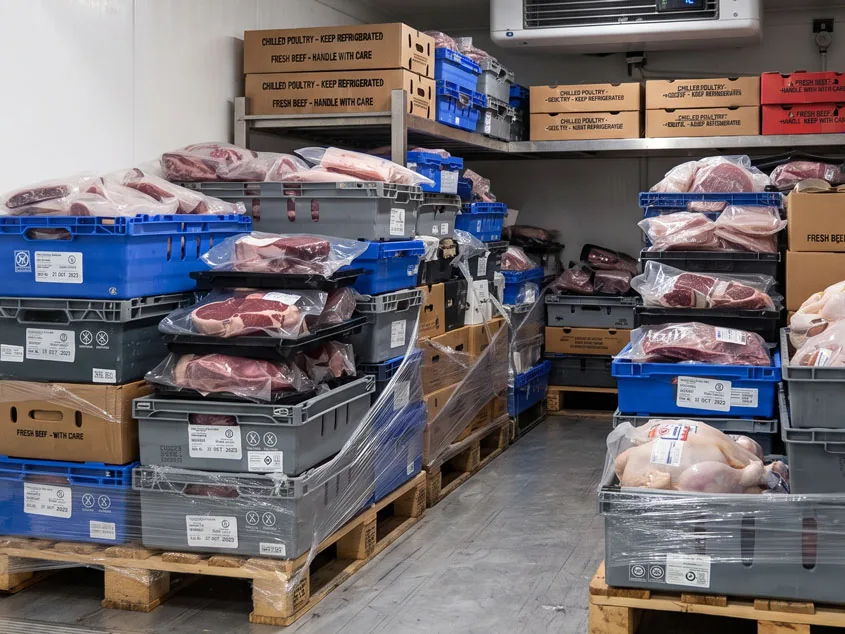 Cámara refrigerada de una distribuidora cárnica con cajas de vacuno, cerdo y pollo apiladas en palés